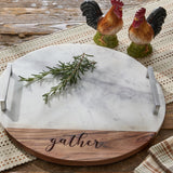Round Gather serving board with a white marble top and a curved wooden base engraved with the word "gather," styled on Toffee & Elm Yarn Basketweave Table Runner with Rooster Day rooster salt and pepper shakers in the background.