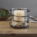 Barbed Wire Rustic Pillar Candle Holder and a lit candle on a wooden surface.