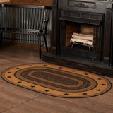 Blackstone Farm Star braided oval rug in black and tan jute placed in front of a black farmhouse fireplace with corrugated metal wall and rustic cabin decor