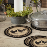 Farmstead Charcoal Poultry Braided 8" Trivet Set of 3 — lifestyle view showing rooster and hen stenciled jute trivets on a whitewashed farmhouse table with a cast aluminum pot and greenery