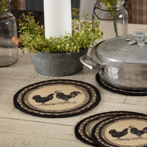 Farmstead Charcoal Poultry Braided 8" Trivet Set of 3 — lifestyle view showing rooster and hen stenciled jute trivets on a whitewashed farmhouse table with a cast aluminum pot and greenery