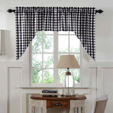 Sable Ann Black and white gingham buffalo check valance curtain hanging on a black rod over a window in a styled room with white wainscoting, a wooden desk, a lamp, and a chair.