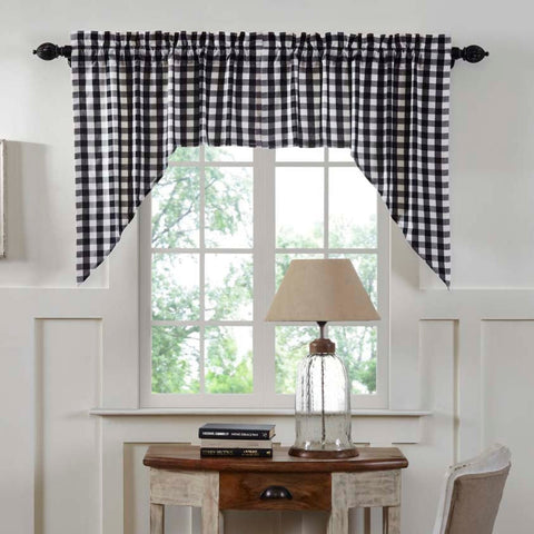 Sable Ann Black and white gingham buffalo check valance curtain hanging on a black rod over a window in a styled room with white wainscoting, a wooden desk, a lamp, and a chair.