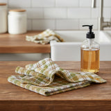 Sage & Mustard Dishcloth Set of 3 plaid patterned fabric with sage green, light mustard yellow, putty brown, and white colors on a farmhouse kitchen counter with a bottle of soap
