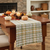Sage & Mustard Plaid Table Runners draped over a wooden dining table, featuring a pattern of sage green, mustard yellow, putty brown and white intersecting stripes.